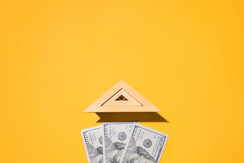 Financing for a new roof shown by wooden roof of toy house and one hundred dollar bills